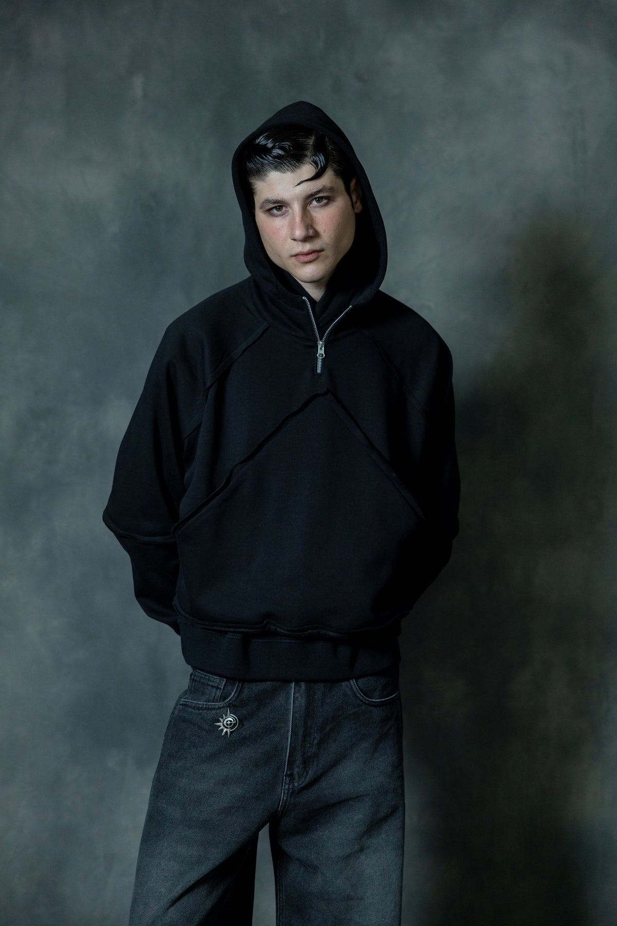 Portrait of a man wearing a premium black cotton zip-neck hoodie with the hood up, showcasing a relaxed fit and minimal urban streetwear aesthetic