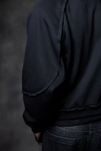 Close-up of black zip neck hoodie showing raw edge sleeve detailing and premium streetwear construction