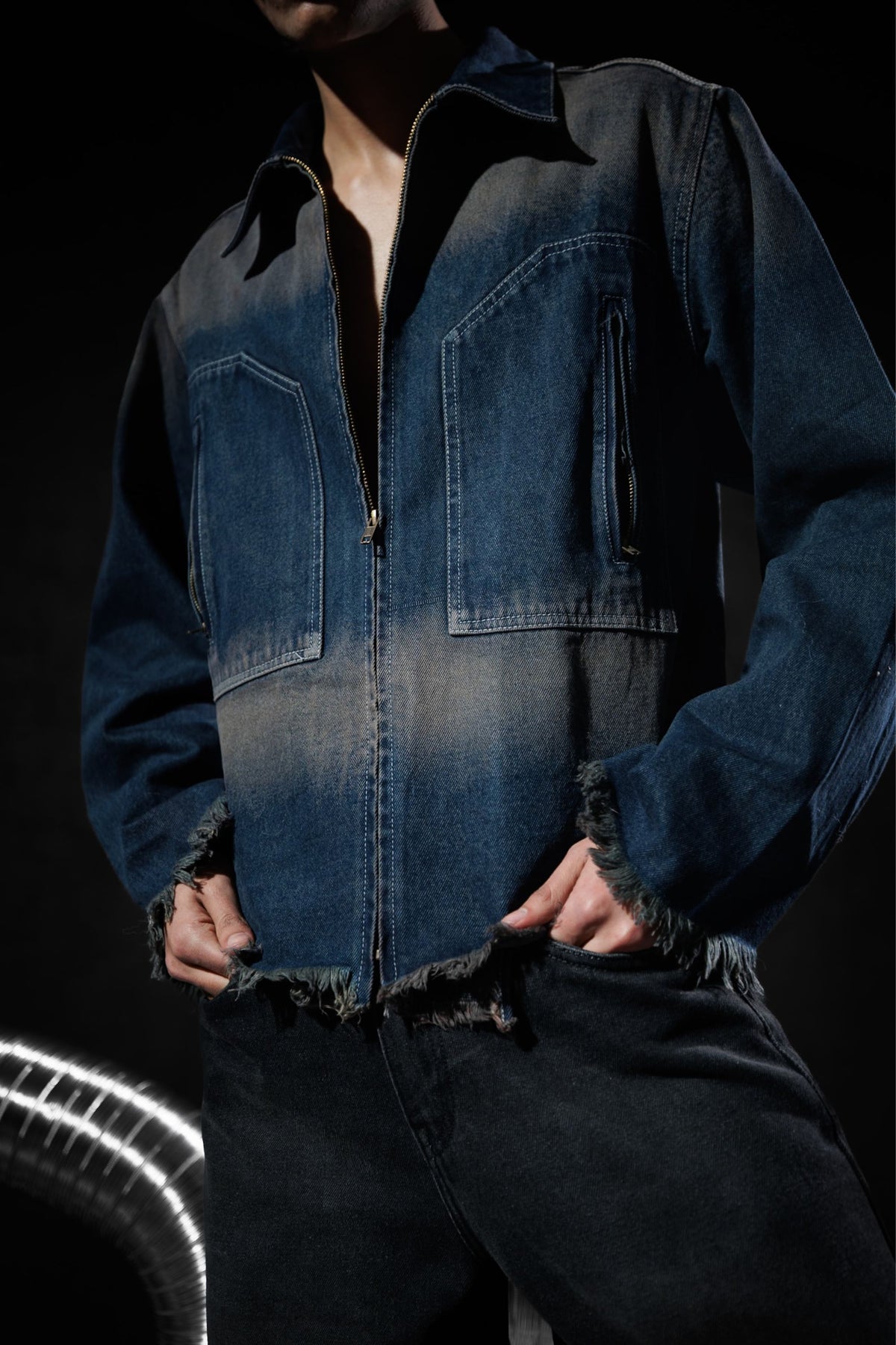 Close up of a blue denim jacket with zipper closure and frayed edges, highlighting modern streetwear design
