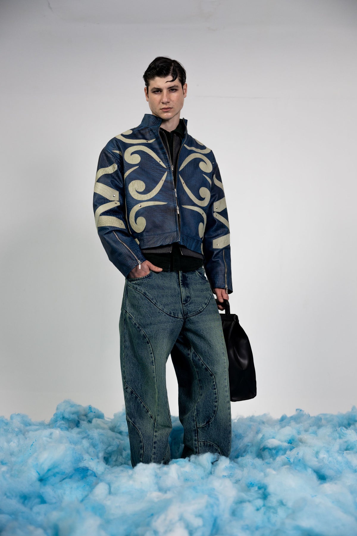 Full body shot of a man wearing a premium blue embossed leather jacket with beige appliqué details, styled for a modern winter streetwear look