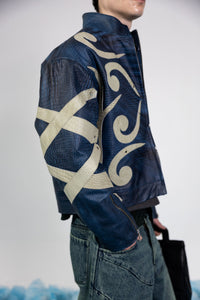 Side profile of men's blue embossed leather jacket, showcasing abstract beige appliqué design on sleeves and metal rivets