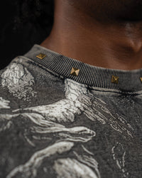 Close-up macro shot of the studded neckline and vintage mythic print on a washed charcoal t-shirt