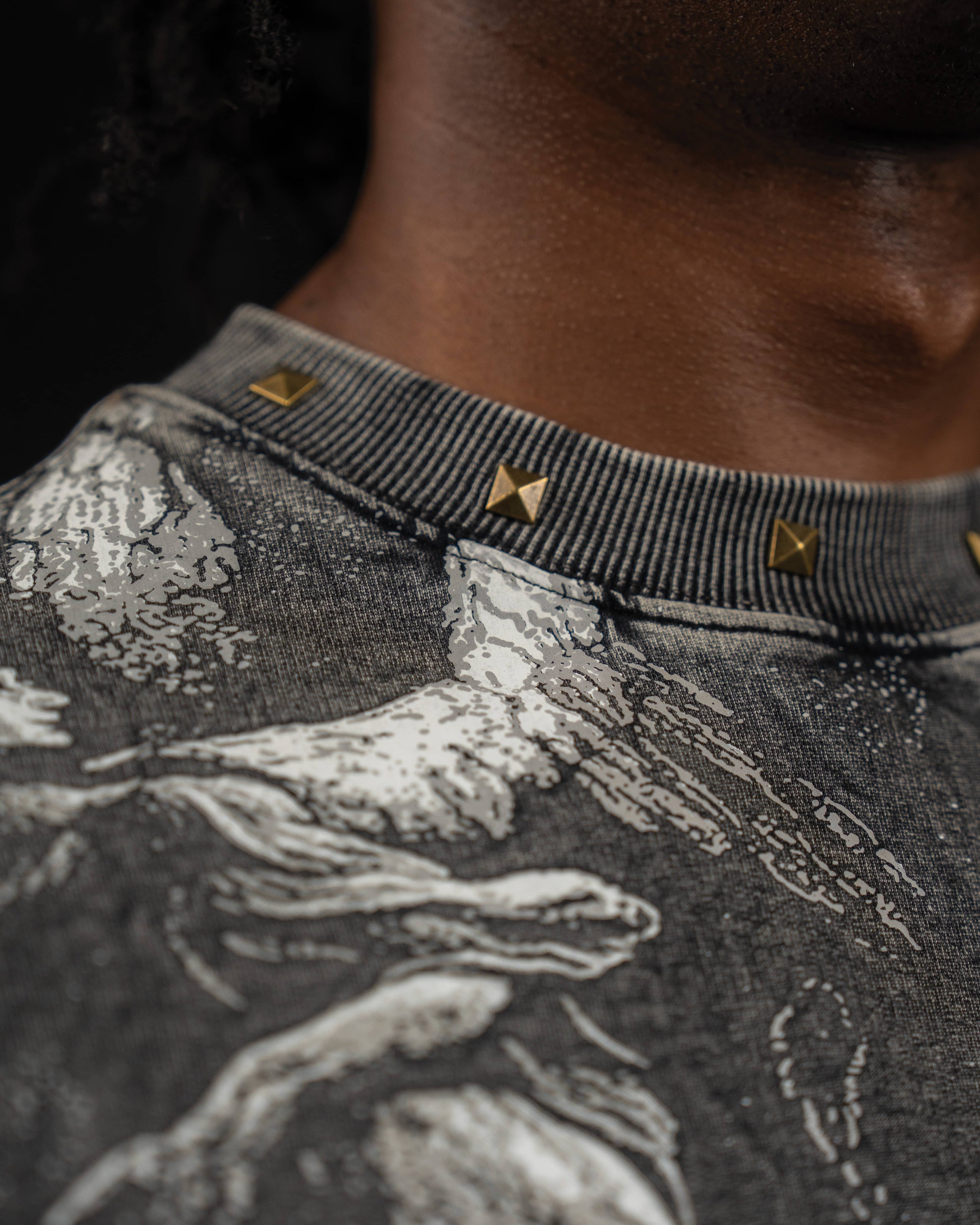 Close-up macro shot of the studded neckline and vintage mythic print on a washed charcoal t-shirt