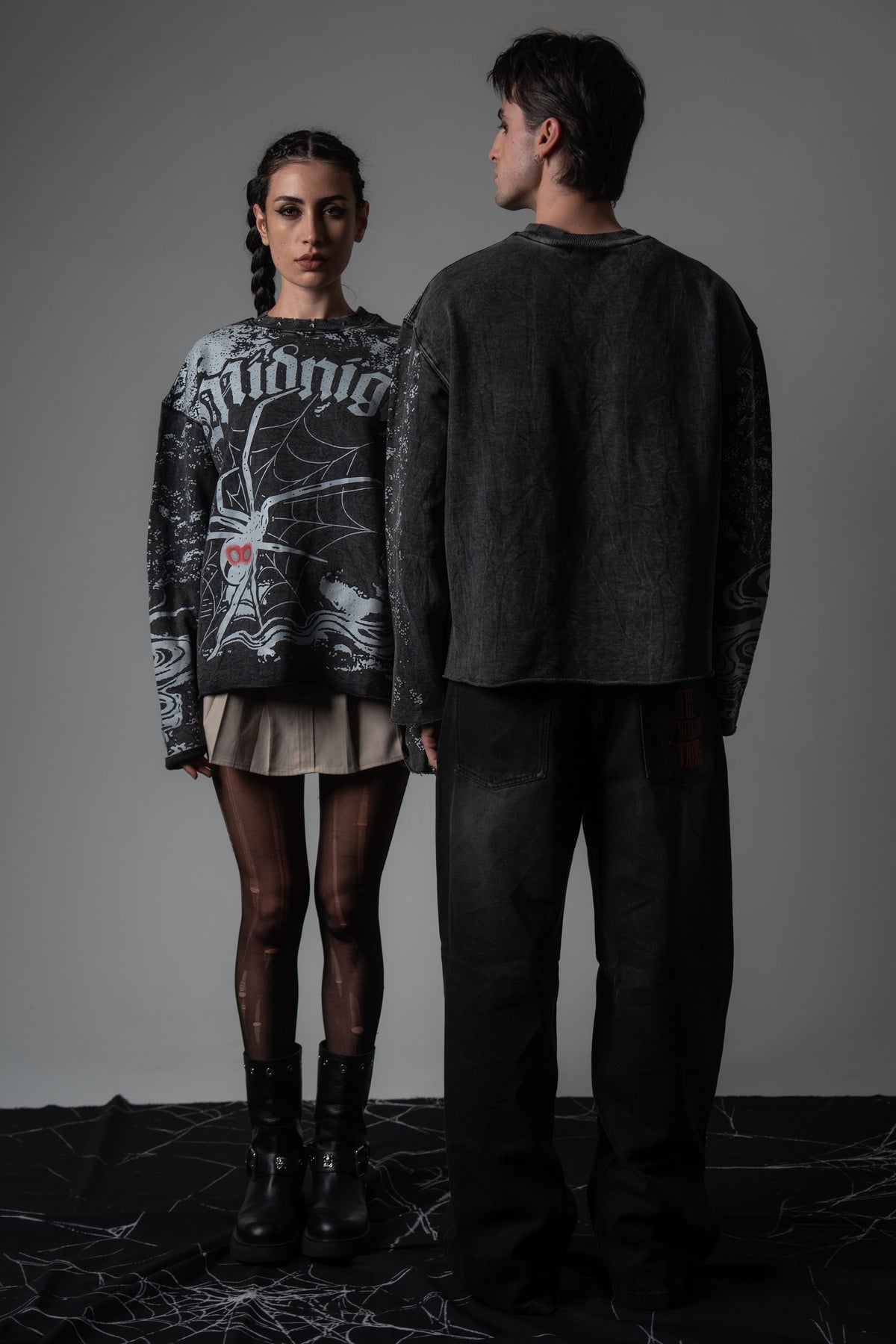Editorial studio shot of a couple wearing matching oversized washed charcoal spiderweb long sleeve tees