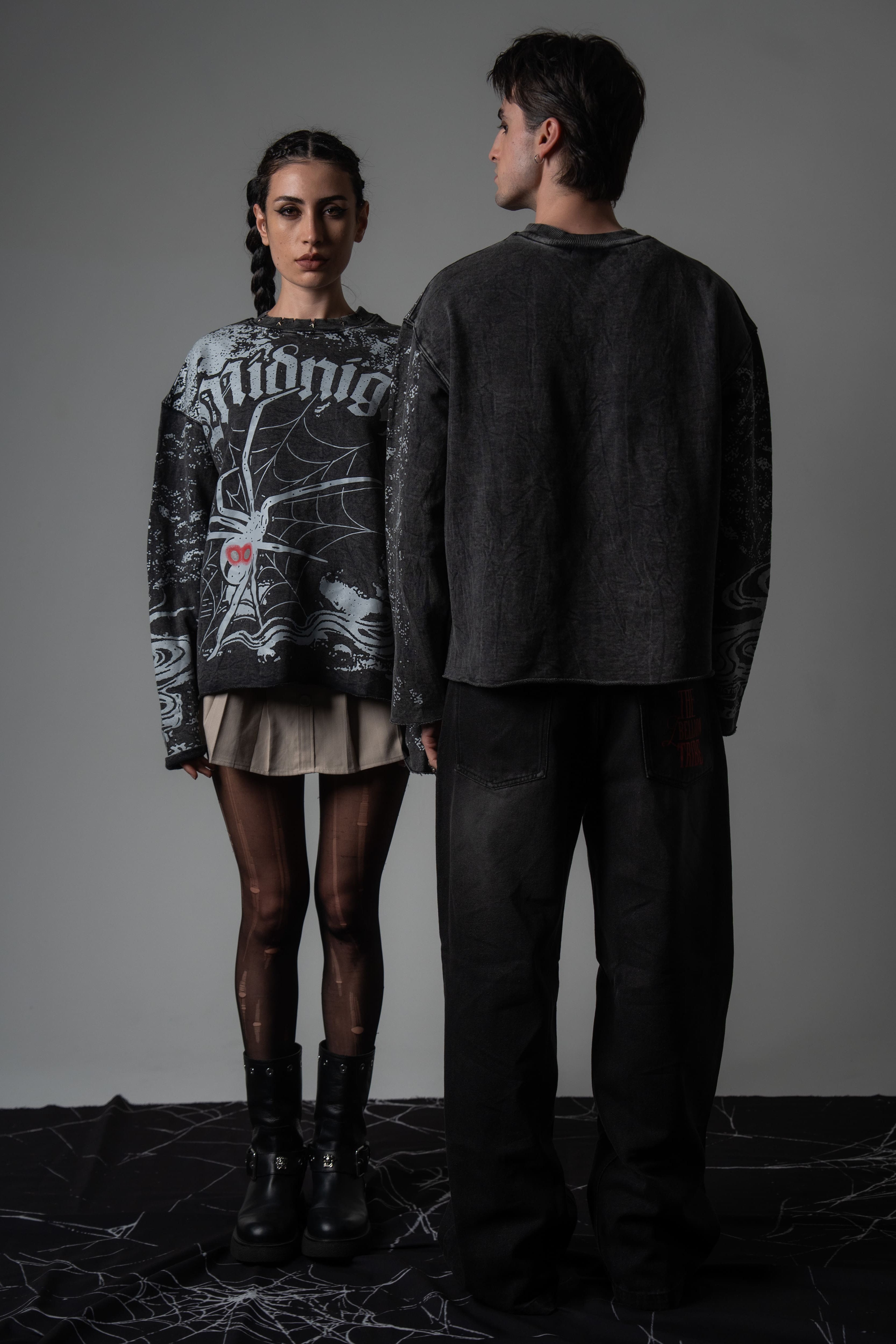 Editorial studio shot of a couple wearing matching oversized washed charcoal spiderweb long sleeve tees