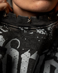 Extreme close-up of the distressed ribbed neckline with metal star stud detailing on a washed charcoal streetwear tee