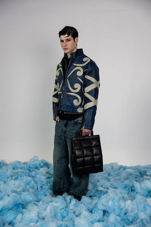 Front view of men's blue crocodile embossed leather jacket featuring contrasting beige abstract appliqué designs and metal rivets