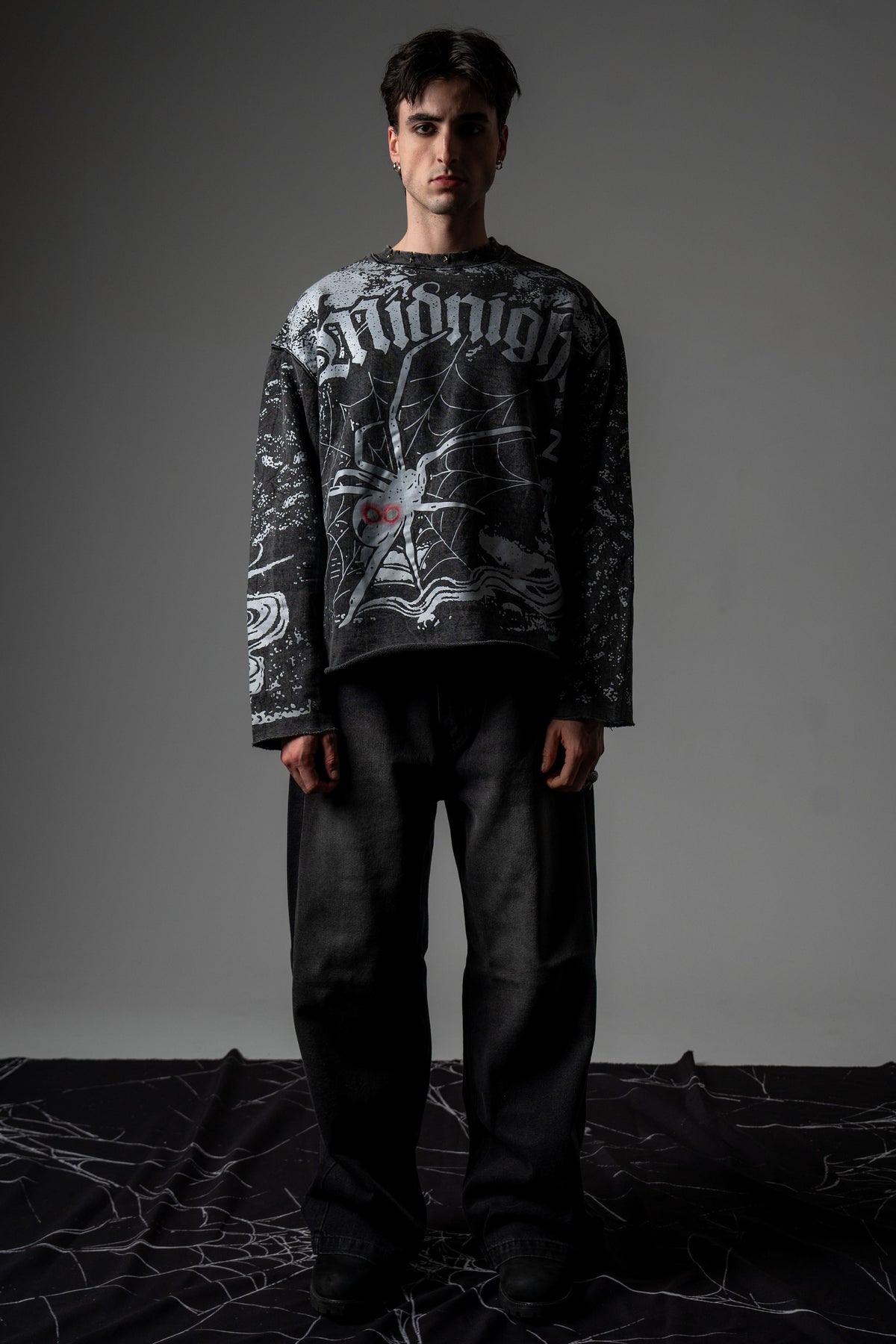 Front full-length studio portrait of a model wearing the washed charcoal SPYCRA.NODE screenprinted long sleeve tee
