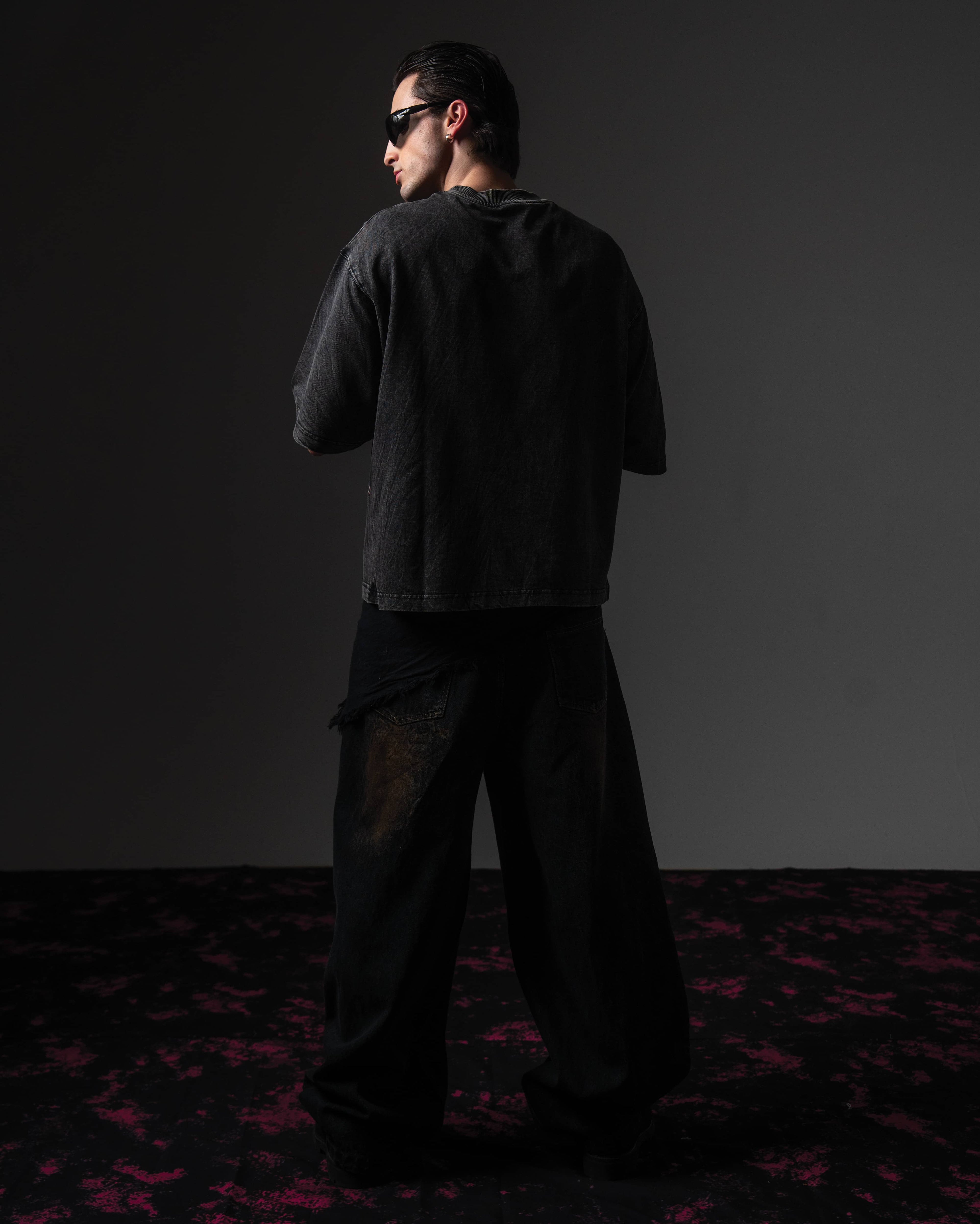 Clean back view of a man wearing an oversized black washed graphic t-shirt showing the distressed finish