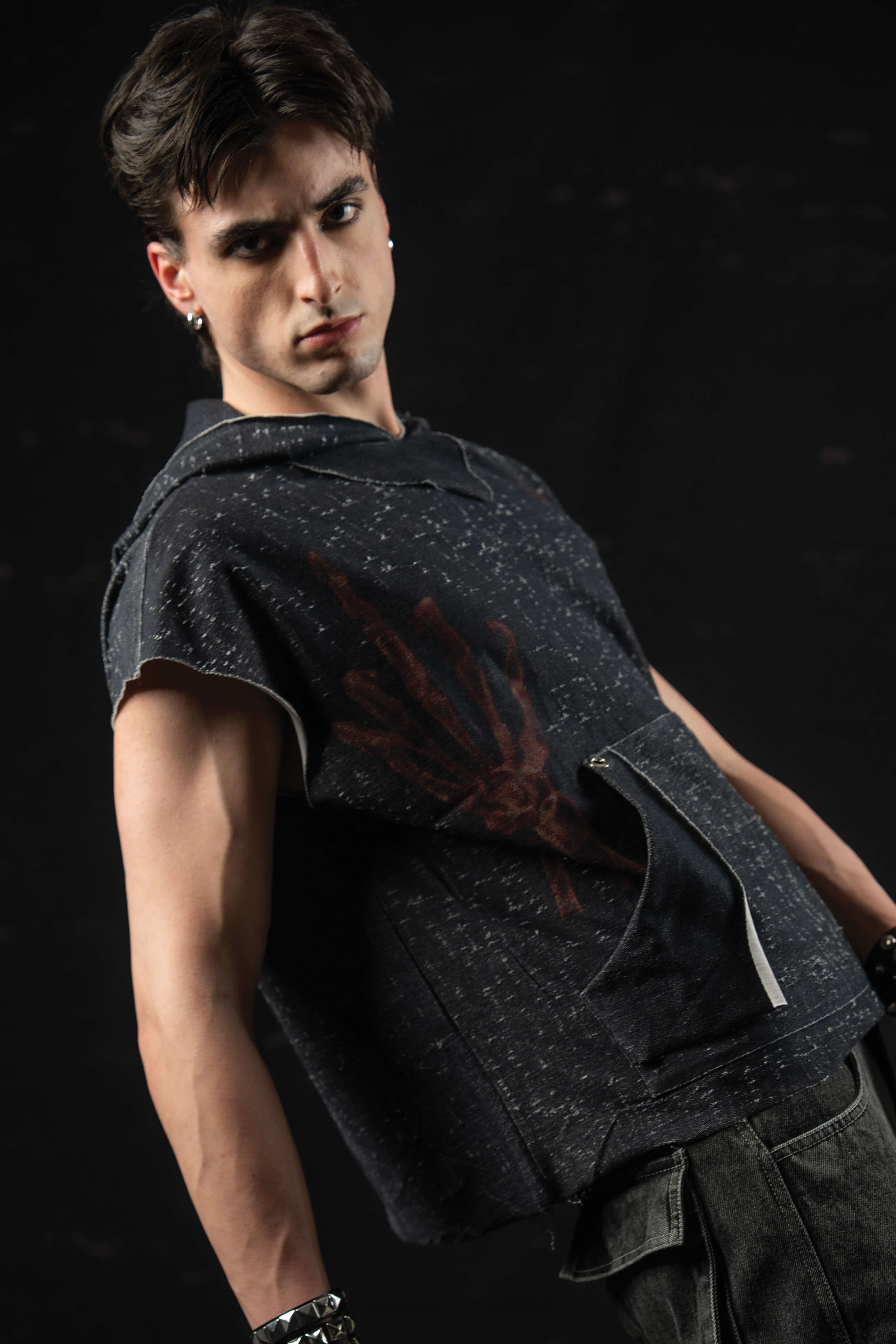 Angled portrait of a model styling a washed charcoal sleeveless hooded graphic tee