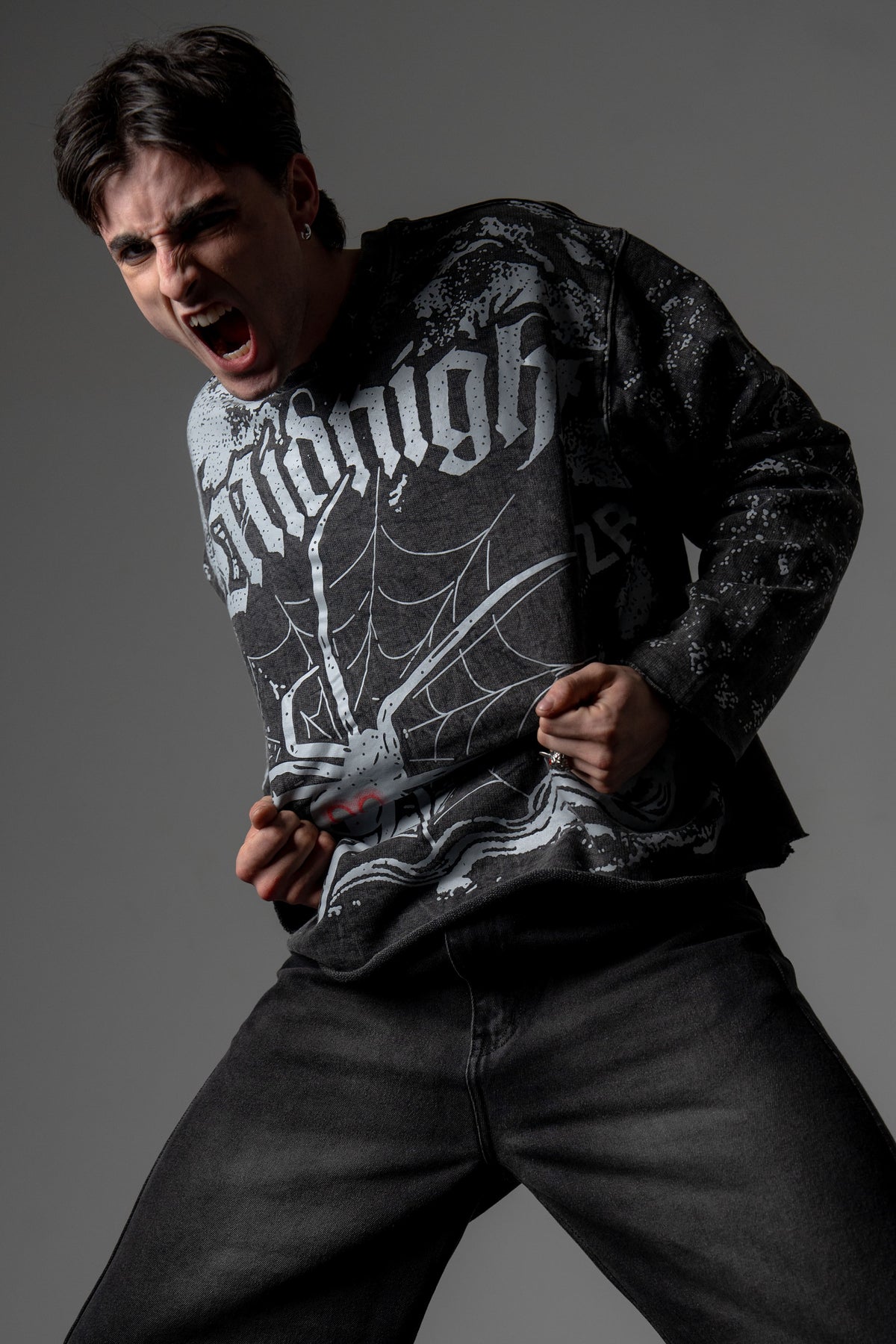 Dynamic action pose of a model styling an oversized washed charcoal spiderweb graphic long sleeve tee