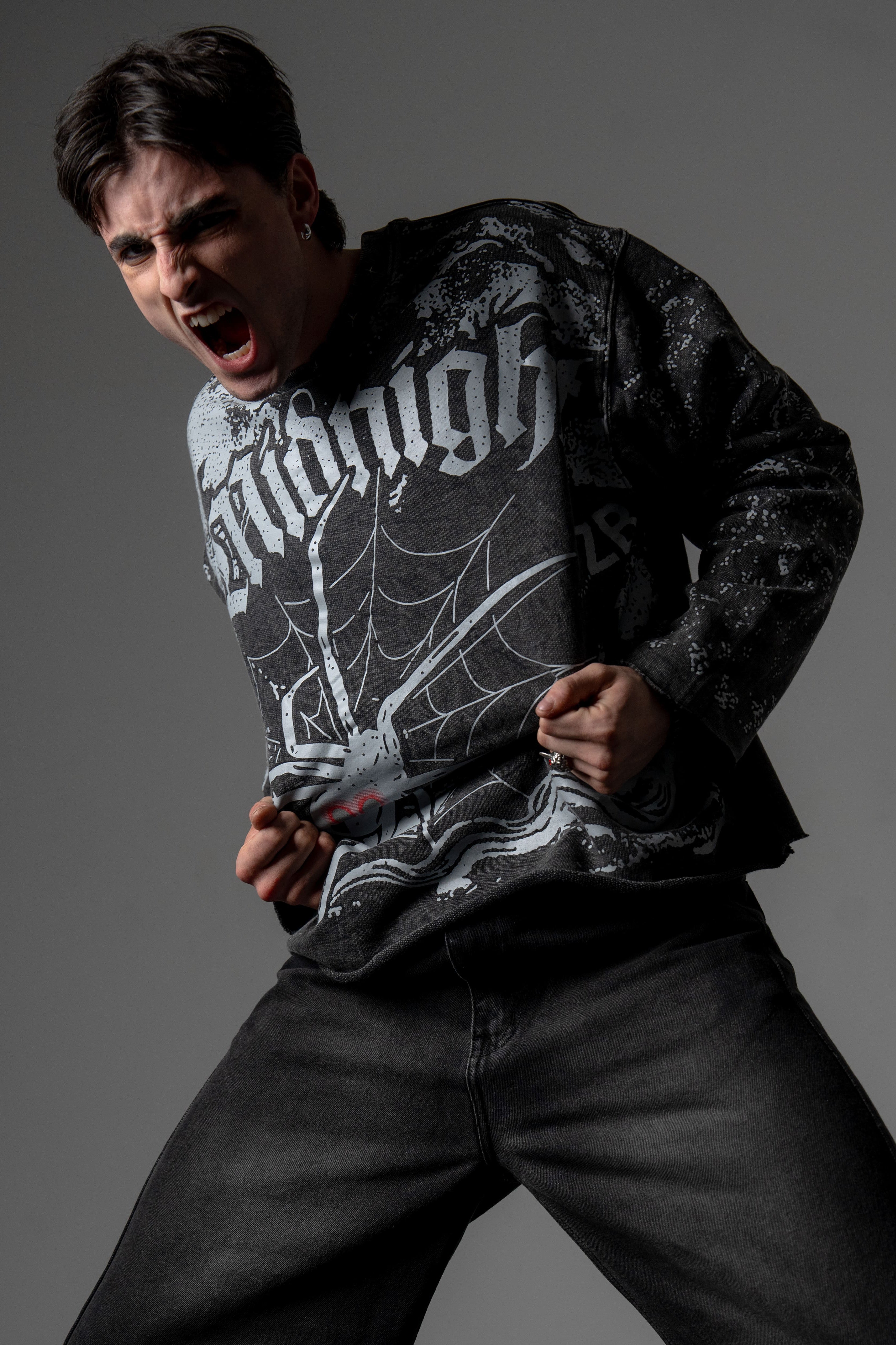 Dynamic action pose of a model styling an oversized washed charcoal spiderweb graphic long sleeve tee