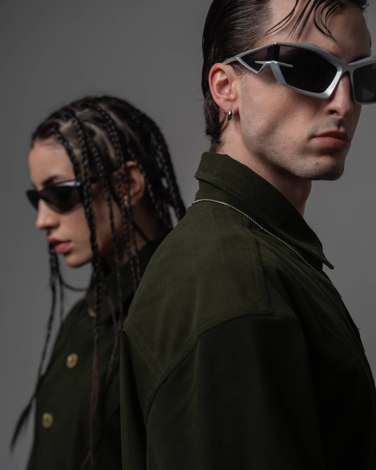 Two models standing back-to-back wearing oversized dark olive textured shirts