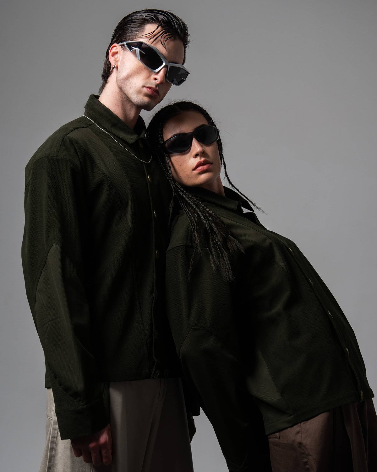 Close-up studio portrait of two models wearing dark olive textured oversized shirts