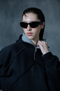 Portrait of a woman wearing a premium cotton black zip-neck hoodie, featuring a layered hood design in a minimal urban streetwear aesthetic