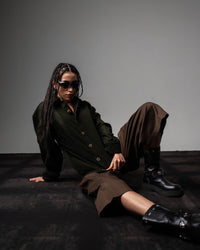 Seated look of a woman styling a dark olive textured oversized button up shirt