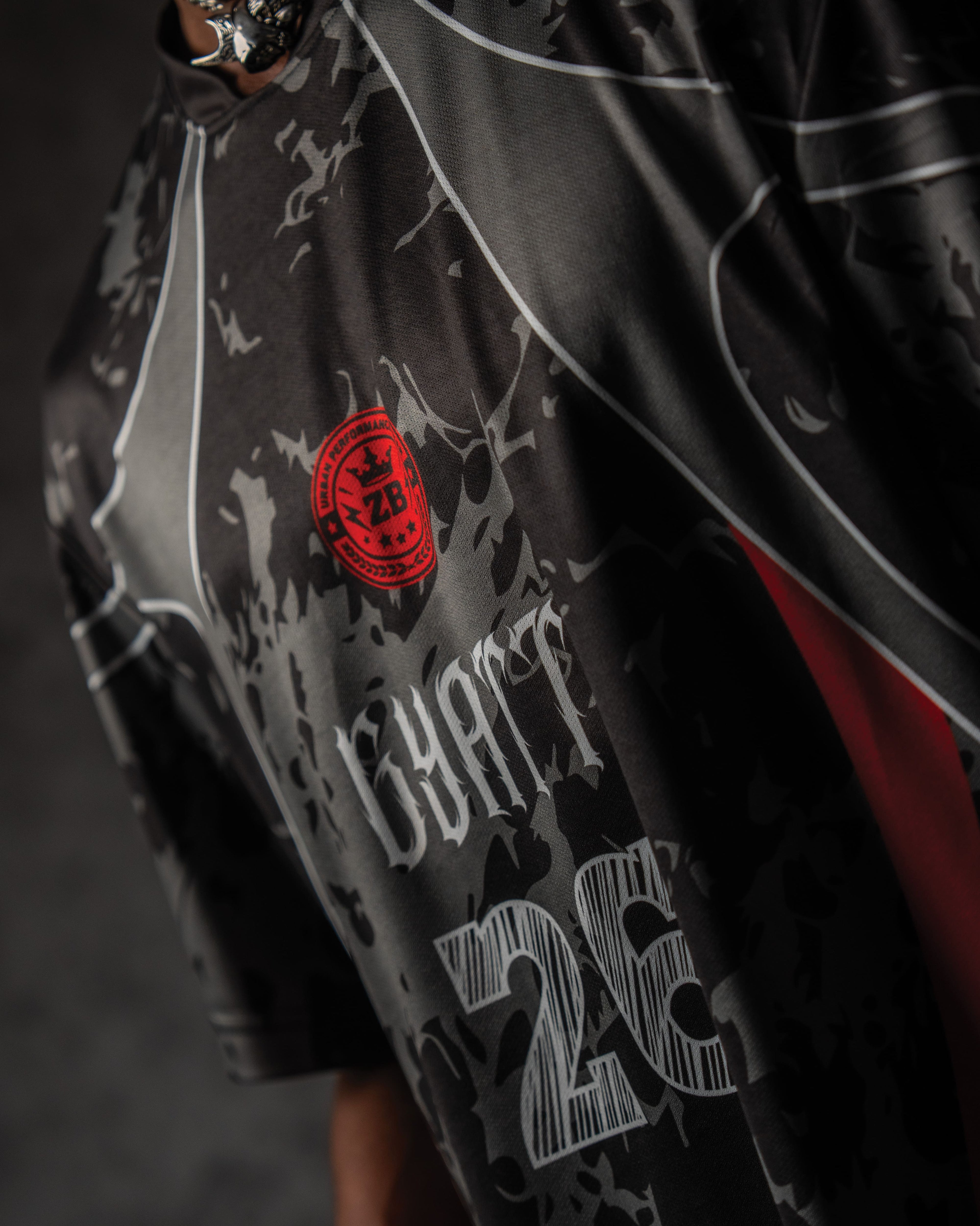 Angled detail shot of the red circular performance logo and distressed gothic typography on a black jersey