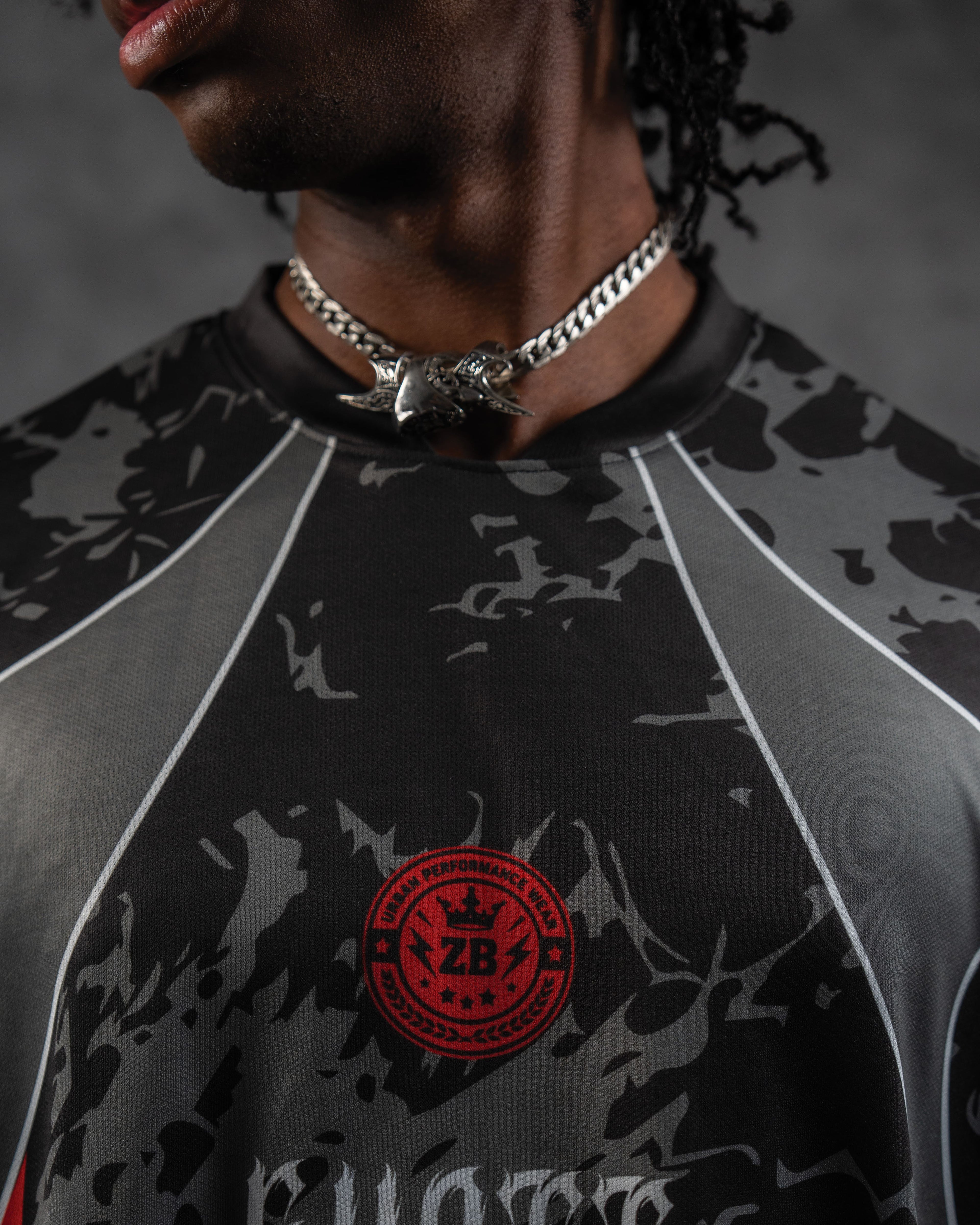 Extreme close-up of the ribbed crewneck collar paired with a silver cuban chain, featuring the red performance crest badge